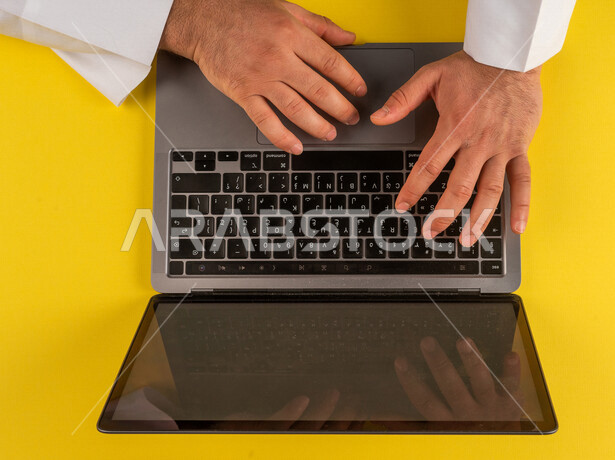 صورة مقربة ليد رجل عربي خليجي سعودي يستخدم الحاسوب المحمول، الكتابة من خلال لوحة المفاتيح ، مدخل بيانات، التسويق والترويج للمواقع الالكترونية، التعليم عن بعد ، استخدام الاجهزة التقنية الحديثة في الاعمال الادارية