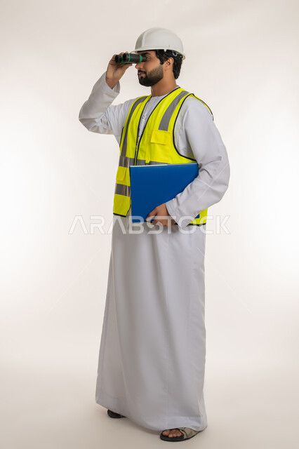 القطاع الهندسي في الإمارات، بورتريه من الجانب لمهندس عربي خليجي إماراتي يرتدي الكندورة والخوذة وسترة الحماية ينظر عبر منظار ثنائي العينين يحمل بيده ملف خاص بالعمل، توسيع مجال الرؤية، التخطيط والبحث للمستقبل، الجسم بالطول الكامل، خلفية بيضاء