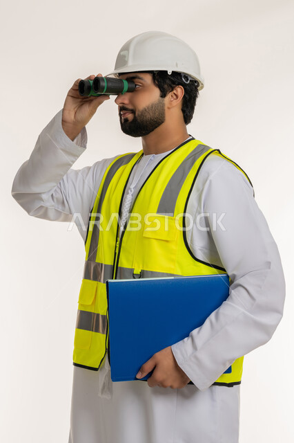 التخطيط والبحث للمستقبل، توسيع مجال الرؤية، الإشراف على المشاريع الهندسية، القطاع الهندسي في الإمارات، بورتريه مقرب لمهندس عربي خليجي إماراتي يرتدي الكندورة والخوذة وسترة الحماية ينظر عبر منظار ثنائي العينين يحمل بيده ملف خاص بالعمل، خلفية بيضاء