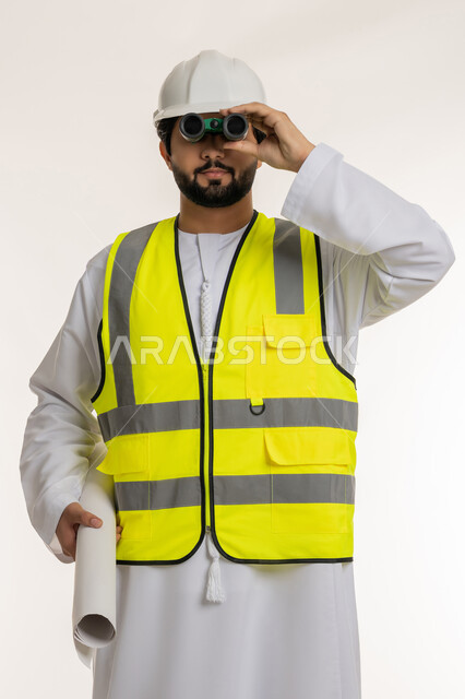 العمل في القطاع الهندسي، المهن والوظائف الشبابية، رؤية الأشياء البعيدة، بورتريه لمهندس عربي خليجي إماراتي يرتدي الكندورة والخوذة وسترة الحماية ينظر من خلال المنظار ثنائي العينين إلى شيء ما يحمل بيده مخطط، متابعة سير المشاريع الهندسية الإعمارية، خلفية بيضاء