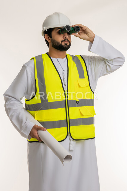Following up on the progress of construction engineering projects, youth professions and jobs, seeing distant objects, portrait of an Arab Gulf Emirati engineer wearing a kandura, helmet and protective vest looking through binoculars at something holding a plan in his hand, white background