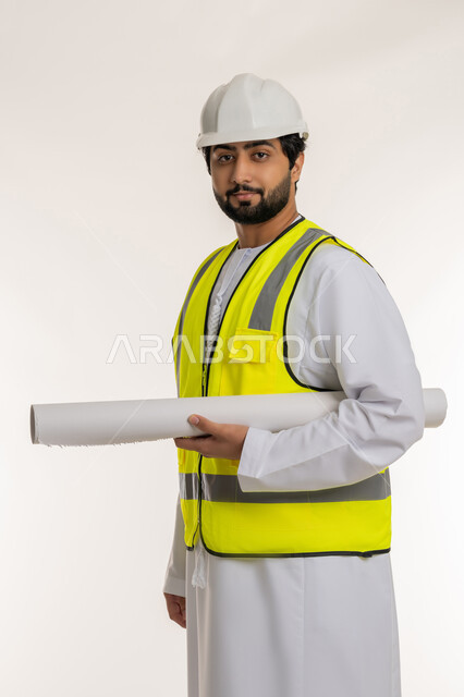Following up on the progress of construction projects, the concept of architectural constructions and engineering, a portrait of an Arab Gulf Emirati engineer wearing a kandura, helmet and protective vest, holding a plan in his hand, looking at the camera with gestures of confidence, youth professions and jobs, white background