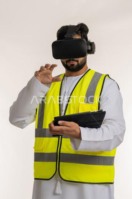 Integrating technology into engineering field in UAE, close up portrait of an Arab Gulf Emirati engineer wearing kandura, work jacket and virtual reality glasses raising his hand to touch holographic elements holding tablet, interacting with virtual engineering, white background