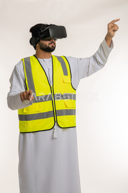 الاندماج مع الهندسة الافتراضية، بورتريه لمهندس عربي خليجي إماراتي يرتدي الكندورة والسترة الخاصة بالعمل ونظارة الواقع الافتراضي يرفع يديه للمس عناصر هولوجرامية، تجسيد ومشاهدة المشاريع الهندسية بالاعتماد على التكنولوجيا، خلفية بيضاء