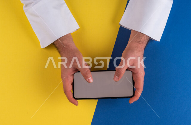 صورة مقربة ليد رجل عربي خليجي سعودي يحمل الهاتف المحمول ، الاستمتاع بمشاهدة الافلام ، لعب الالعاب الالكترونية ، متابعة الدروس التعليمية ،استخدام التقنيات الحديثة