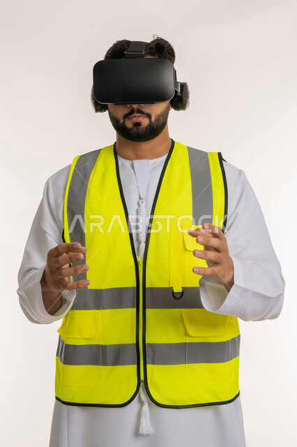الاندماج مع الهندسة الافتراضية، بورتريه مقرب لمهندس عربي خليجي إماراتي يرتدي الكندورة والسترة الخاصة بالعمل ونظارة الواقع الافتراضي يرفع يديه لمحاولة تحجيم العناصر الهولوجرامية والإمساك بها، تجسيد ومشاهدة المشاريع الهندسية بالاعتماد على التكنولوجيا، خلفية بيضاء
