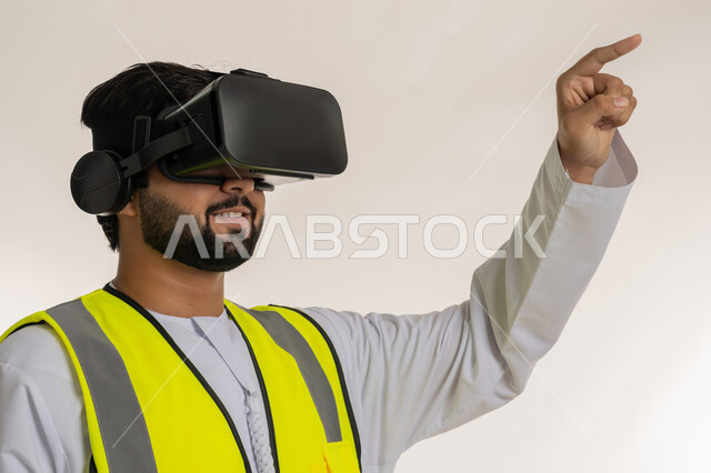 رؤية مستقبلية 2030، التفاعل مع الهندسة الافتراضية، بورتريه مقرب من الجانب لمهندس عربي خليجي إماراتي يرتدي الكندورة والسترة الخاصة بالعمل ونظارة الواقع الافتراضي يرفع إصبع السبابة للمس عناصر هولوجرامية، دمج التكنولوجيا بالمجالات الهندسية، خلفية بيضاء