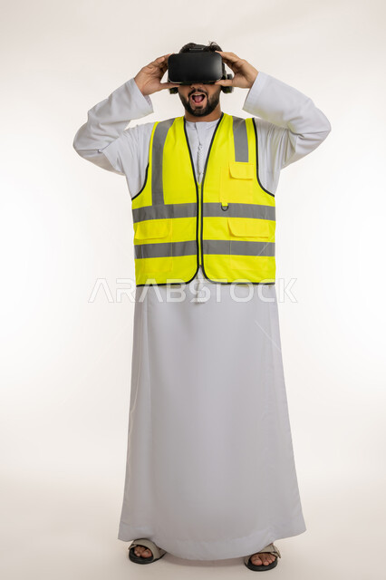 تطور المجال الهندسي في الإمارات، فتح الفم بإيماءات الدهشة والذهول، بورتريه لمهندس عربي خليجي إماراتي يرتدي الكندورة والسترة الخاصة بالعمل ونظارة الواقع الافتراضي، مشاهدة المشاريع الهندسية بالاعتماد على التكنولوجيا، الجسم بالطول الكامل، خلفية بيضاء