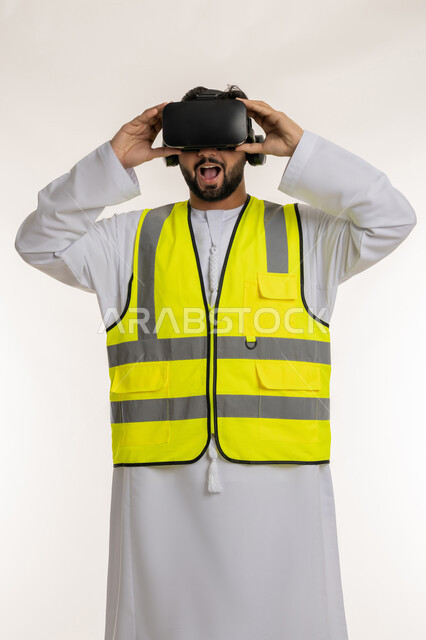 فتح الفم بإيماءات الدهشة والذهول، التفاعل مع الهندسة الافتراضية، بورتريه لمهندس عربي خليجي إماراتي يرتدي الكندورة والسترة الخاصة بالعمل ونظارة الواقع الافتراضي، تطور المجال الهندسي في الإمارات، مشاهدة المشاريع الهندسية بالاعتماد على التكنولوجيا، خلفية بيضاء