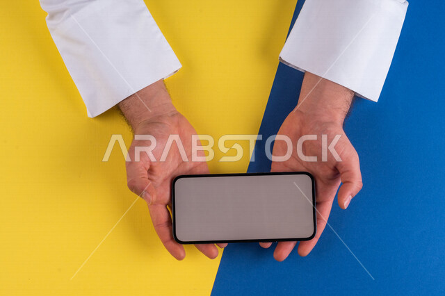صورة مقربة ليد رجل عربي خليجي سعودي يحمل الهاتف المحمول ، الاستمتاع بمشاهدة الافلام ، لعب الالعاب الالكترونية ، متابعة الدروس التعليمية ،استخدام التقنيات الحديثة