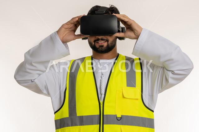 التفاعل مع الهندسة الافتراضية، بورتريه مقرب لمهندس عربي خليجي إماراتي يرتدي الكندورة والسترة الخاصة بالعمل ونظارة الواقع الافتراضي، تطور المجال الهندسي في الإمارات العربية المتحدة، مشاهدة المشاريع الهندسية بالاعتماد على التكنولوجيا، خلفية بيضاء