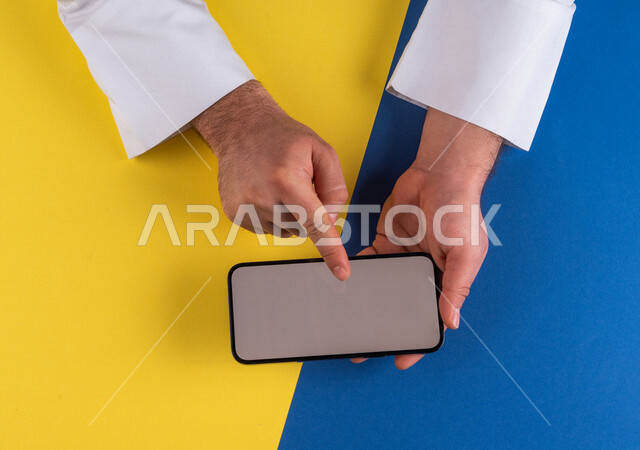 صورة مقربة ليد رجل عربي خليجي سعودي يحمل الهاتف المحمول ، الاستمتاع بمشاهدة الافلام ، لعب الالعاب الالكترونية ، متابعة الدروس التعليمية ،استخدام التقنيات الحديثة