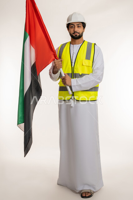 متابعة الأعمال الهندسية، الفخر والاعتزاز بالانتماء للوطن، ذكرى قيام الاتحاد 2 ديسمبر 1971، بورتريه لمهندس عربي خليجي إماراتي يرتدي الكندورة والخوذة وسترة الحماية يحمل علم دولة الإمارات المتحدة، يوم العلم الإماراتي 3 نوفمبر، الجسم بالطول الكامل، خلفية بيضاء