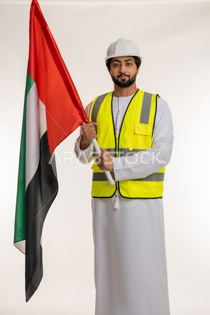 الاحتفال بيوم العلم الإماراتي 3 نوفمبر، ذكرى قيام الاتحاد 2 ديسمبر 1971، بورتريه لمهندس عربي خليجي إماراتي يرتدي الكندورة والخوذة وسترة الحماية يحمل بيده علم دولة الإمارات المتحدة، إيماءات الفخر والاعتزاز بالانتماء للوطن، إدارة الأعمال الهندسية، خلفية بيضاء