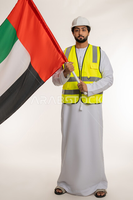 الفخر والاعتزاز بالانتماء للوطن، ذكرى قيام الاتحاد 2 ديسمبر 1971، بورتريه لمهندس عربي خليجي إماراتي يرتدي الكندورة والخوذة وسترة الحماية يحمل علم دولة الإمارات المتحدة، يوم العلم الإماراتي 3 نوفمبر، إدارة الأعمال الهندسية، الجسم بالطول الكامل، خلفية بيضاء