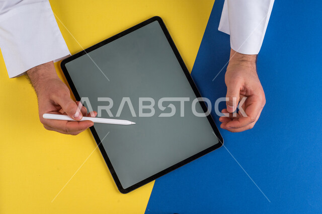 A close-up of the hand of a Saudi Arabian Gulf man using a tablet device, using a tablet pen to take notes on work, explaining work steps, marketing for a website, drawing pictures and designs, using modern technologies in administrative work