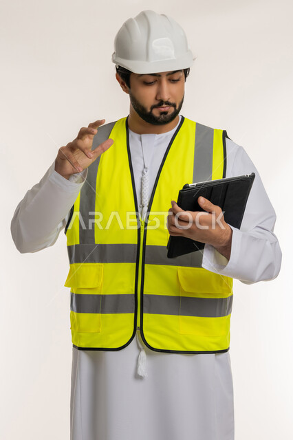 التأكد من سير الأعمال بالشكل المطلوب والصحيح، بورتريه لمهندس عربي خليجي إماراتي يرتدي الكندورة والخوذة وسترة الحماية يقوم باستخدام الجهاز اللوحي، الأجهزة التقنية الحديثة، تدوين و تسجيل الملاحظات, كتابة آخر المستجدات حول المشروع، خلفية بيضاء