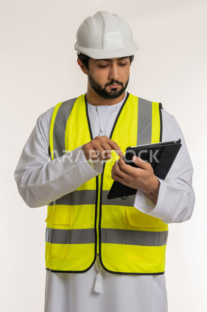 كتابة آخر المستجدات حول المشروع، التأكد من سير الأعمال بالشكل المطلوب والصحيح، بورتريه لمهندس عربي خليجي إماراتي يرتدي الكندورة والخوذة وسترة الحماية يقوم باستخدام الجهاز اللوحي، الأجهزة التقنية الحديثة، تدوين و تسجيل الملاحظات, خلفية بيضاء