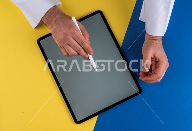 صورة مقربة ليد رجل عربي خليجي سعودي يستخدم جهاز التابلت ، استخدام قلم التابلت لتدوين ملاحظات خاصة بالعمل ،شرح خطوات العمل ، التسويق لموقع الكتروني ،رسم الصور والتصاميم ،استخدام التقنيات الحديثة في الاعمال الادارية