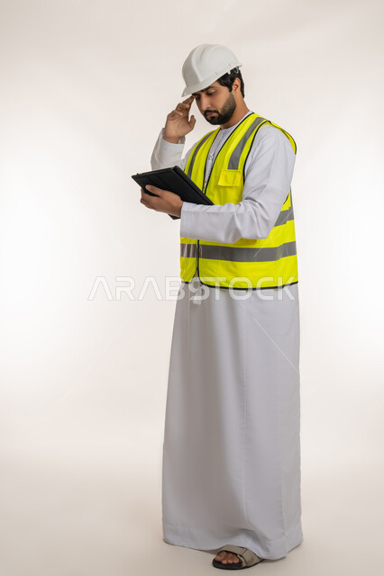تدوين وتسجيل الملاحظات, إدارة المشاريع الهندسية، بورتريه لمهندس عربي خليجي إماراتي يرتدي الكندورة وسترة الحماية يقوم باستخدام الجهاز اللوحي يضع يده على رأسه بإيماءات التفكير، محاولة تذكر شيء ما، الأجهزة التقنية الحديثة، الجسم بالطول الكامل، خلفية بيضاء