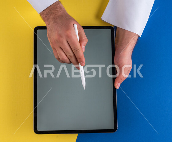 A close-up of the hand of a Saudi Arabian Gulf man using a tablet device, using a tablet pen to take notes on work, explaining work steps, marketing for a website, drawing pictures and designs, using modern technologies in administrative work