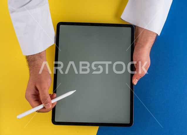 صورة مقربة ليد رجل عربي خليجي سعودي يستخدم جهاز التابلت ، استخدام قلم التابلت لتدوين ملاحظات خاصة بالعمل ،شرح خطوات العمل ، التسويق لموقع الكتروني ،رسم الصور والتصاميم ،استخدام التقنيات الحديثة في الاعمال الادارية
