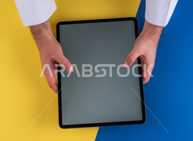 صورة مقربة ليد رجل عربي خليجي سعودي يستخدم جهاز التابلت، الاستمتاع بمشاهدة الافلام ، لعب الالعاب الالكترونية ، متابعة الدروس التعليمية ،استخدام التقنيات الحديثة