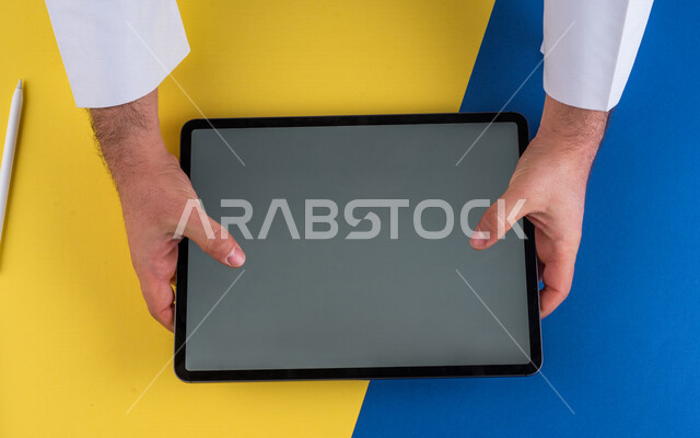 صورة مقربة ليد رجل عربي خليجي سعودي يستخدم جهاز التابلت، الاستمتاع بمشاهدة الافلام ، لعب الالعاب الالكترونية ، متابعة الدروس التعليمية ،استخدام التقنيات الحديثة