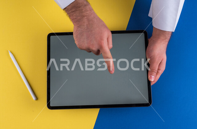 صورة مقربة ليد رجل عربي خليجي سعودي ينقر على شاشة جهاز التابلت، شرح خطوات العمل ،القيام بعمليات التسويق الالكتروني ، التجارة الالكترونية ،تصفح المواقع الالكترونية ، استخدام الاجهزة التقنية الحديثة في الاعمال الادارية
