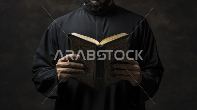 تلاوة سور القرآن الكريم, العبادة والتقرب إلى الله تعالى, التمعن بالآيات القرآنية والتفكر بها، أداء الفرائض الدينية الإسلامية، مفهوم التعبد في بيوت الرحمن, بورتريه مقرب لرجل عربي خليجي سعودي يرتدي الثوب التقليدي يمسك بيده المصحف الشريف, خلفية رمادية
