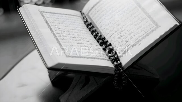 قراءة وتلاوة المصحف الشريف، العبادة والتقرب إلى الله تعالى، صورة مقربة بالابيض و الاسود للقرآن الكريم على حامل خشبي في المسجد، التعبد والاعتكاف في بيت الله الحرام، تدبر الآيات القرآنية والتفكر بها, الالتزام بالورد اليومي