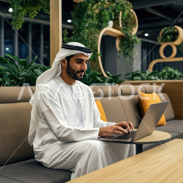 إدارة شؤون الأعمال وتنظيمها عبر الأجهزة التقنية الحديثة، استخدام التكنولوجيا والتقنيات المتطورة، إنجاز مهام العمل عن بعد، رجل عربي خليجي اماراتي يرتدي الكندورة والغترة البيضاء يجلس على الأريكة في إحدى المقاهي الراقية ويستخدم الحاسوب المحمول