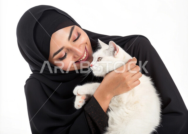 Feeling happy while having fun playing with cat, close-up portrait of smiling Saudi Arabian Gulf woman wearing hijab and abaya holding a gray pet cat, concept of kindness and compassion towards animals, positive impact of owning and raising pets, white background