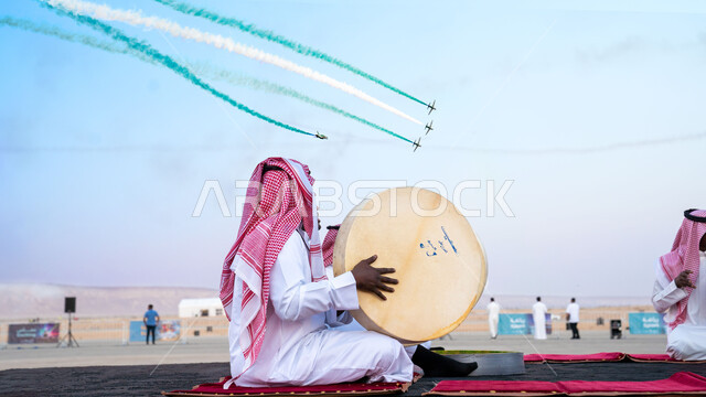 تزيين السماء بدخان ملون، تحليق الطيران الحربي في سماء المملكة العربية السعودية في ذكرى يوم العلم 11 مارس، رجل عربي خليجي سعودي يرتدي الشماغ والثوب التقليدي يقوم بالاحتفال وقرع الطبول، العرض الجوي للطائرات في احتفالات اليوم الوطني السعودي 23 سبتمبر