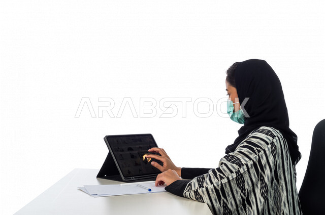 Portrait of a Saudi Arabian Gulf woman wearing a protective mask, using the tablet to browse the Internet, e-marketing through the tablet, adhering to precautions to prevent corona virus