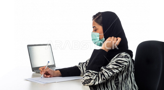 بورتريه لسيدة اعمال عربية خليجية سعودية، انجاز مهام العمل من خلال الحاسوب المحمول، ارتداء الكمامة للوقاية من فايروس كورونا، تسجيل الملاحظات على الورق، اجهزة تقنية حديثة، خلفية بيضاء