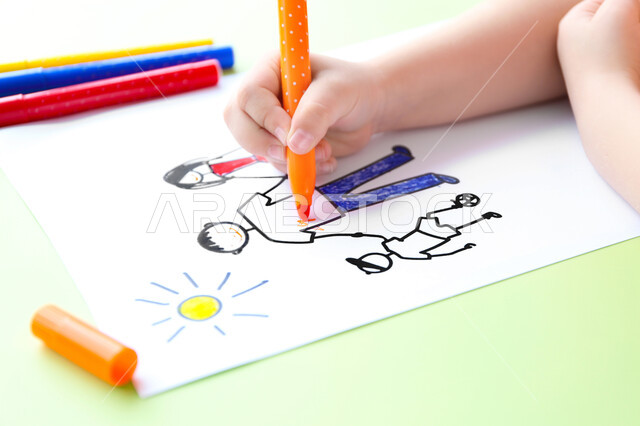 Activities that help develop mental and intellectual abilities and skills, a close-up image of the hand of a Saudi Arabian Gulf boy in kindergartens and nurseries holding a pen in his hand and coloring drawings, art classes and sessions in kindergartens in the Kingdom of Saudi Arabia