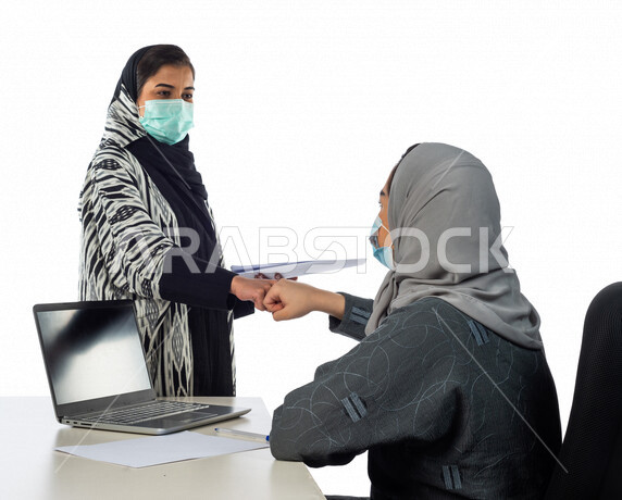 Portrait of two Gulf Arab women shaking hands inside the company, a work agreement between businesswomen, a successful deal, cooperation at work, achieving work goals, wearing a muzzle to prevent corona virus