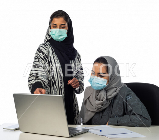 بورتريه لسيدة اعمال عربية خليجية سعودية تجلس امام الحاسوب المحمول، بجانبها موظفة عربية خليجية سعوية، فريق عمل خليجي سعودي، مناقشة وتنظيم الاعمال، ارتداء الكمامة للوقاية من فايروس كورونا