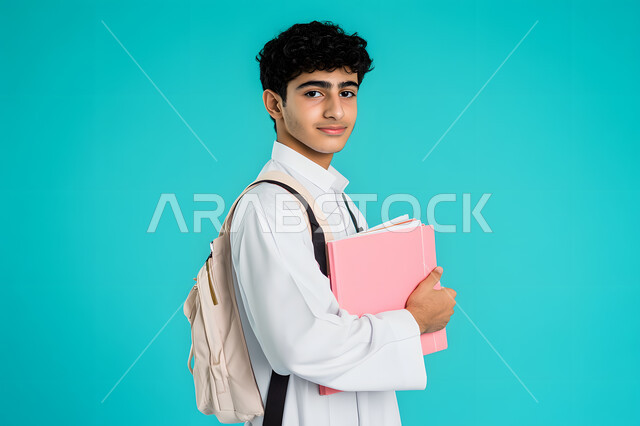 النظر بإيماءات السعادة والسرور, الاستعداد للعام الجامعي الجديد, التعليم العالي في الجامعات والكليات الأكاديمية في سلطنة عمان,  بورتريه لطالب عربي خليجي عسعودي يرتدي الثوب التقليدي والكمة يحمل بيديه الكتب,  خلفية زرقاء