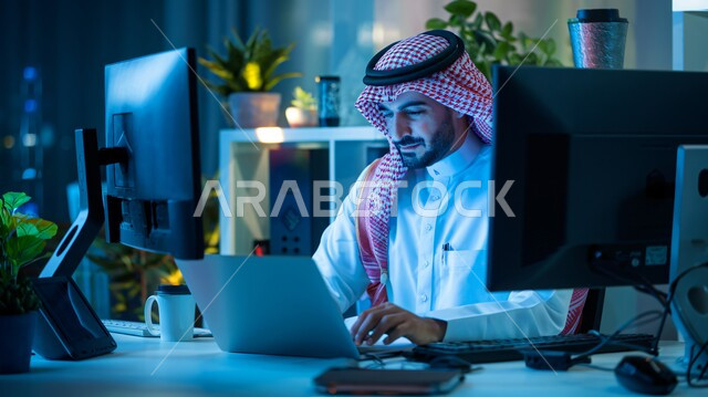 دمج العمل مع التقنية والتكنولوجيا، مهن ووظائف ادارية مكتبية، إدارة شؤون الأعمال وتنظيمها عبر الاجهزة التقنية، رجل اعمال عربي خليجي سعودي يرتدي الشماغ والثوب التقليدي  يعمل على الحاسوب المحمول داخل المكتب
