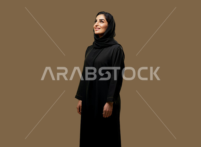 مفهوم الأناقة والأنوثة, تعابير السرور والسعادة، التقاط صور شخصية للوثائق الرسمية، بورتريه لامرأة عربية خليجية سعودية ترتدي الحجاب والعباءة تنظر إلى مكان ما بايماءات الثقة بالنفس, الاهتمام بالمظهر الخارجي، خلفية بنية