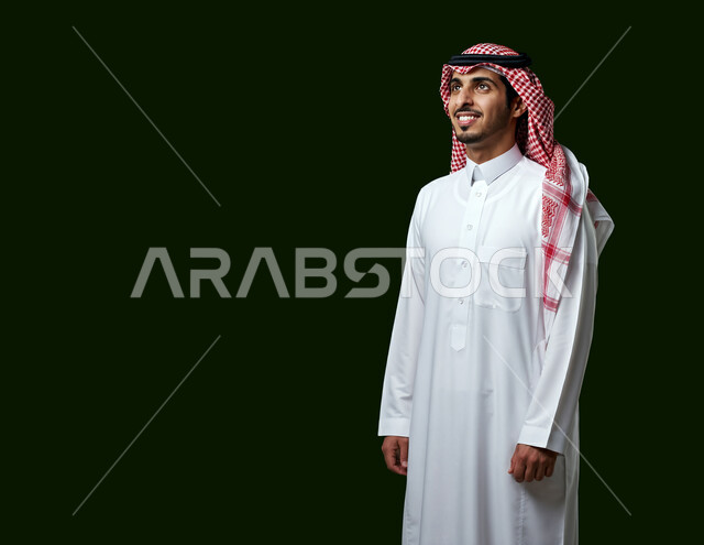 The concept of elegance and masculinity, self-confidence and interest in appearance, portrait of a young Saudi Arabian Gulf man wearing traditional thobe and shemagh looking somewhere with expressions of happiness and pleasure, green background