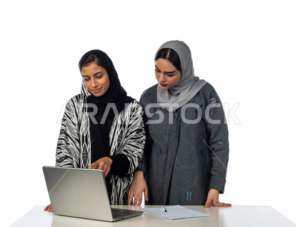 Portrait of a Saudi Arabian Gulf businesswoman sitting in front of her laptop, next to her a Saudi Arabian Gulf employee, a Saudi Gulf work team, discussing and organizing business, achieving work goals