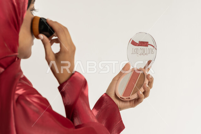 الاهتمام بالمظهر الخارجي, مفهوم التزين والتجمل, استخدام المساحيق التجميلية, التسويق لمستحضرات التجميل, بورتريه مقرب من الخلف لامرأة عربية خليجية إماراتية محجبة ترتدي العباءة الحمراء تستعمل علبة وفرشاة أحمر الخدود, شابة سعودية تضع المكياج, خلفية بيضاء