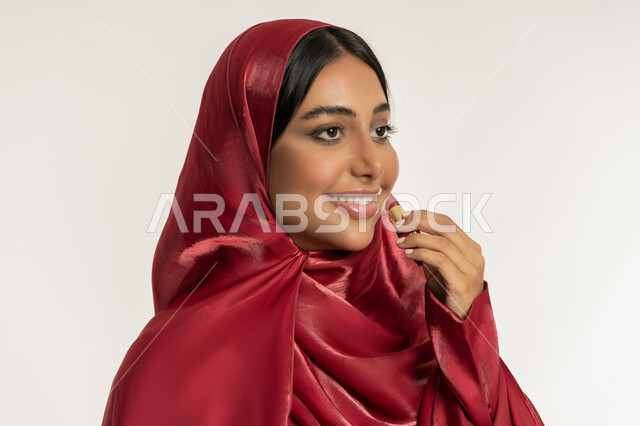 استعمال المستحضرات التجميلية, مفهوم التزين والتجمل, الترويج لمنتجات و مساحيق التجميل, العناية بالجمال والمظهر الخارجي, بورتريه مقرب لامرأة عربية خليجية إماراتية محجبة ترتدي العباءة الحمراء تضع أحمر شفاه, شابة سعودية تقوم بوضع المكياج, خلفية بيضاء