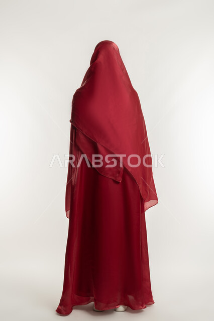 مفهوم الاهتمام بالأناقة والمظهر الخارجي, أزياء محجبات عصرية حديثة, بورتريه من الخلف لامرأة عربية خليجية إماراتية ترتدي العباءة الحمراء تقف باستقامة واعتدال, شابة سعودية أنيقة, الجسم بالطول الكامل, خلفية بيضاء