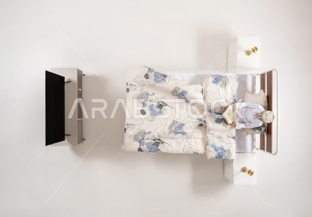 القراءة والإطلاع والاستعداد للعالم الدراسي الجديد، بورتريه علوي عامودي لولد عربي خليجي عماني يرتدي الدشداشة والكمة يستلقي على سريح مريح يقوم بقراءة كتاب، كتب علمية وروايات ثقافية، تنمية المهارات الذهنية وممارسة هواية المطالعة، خلفيه بيضاء