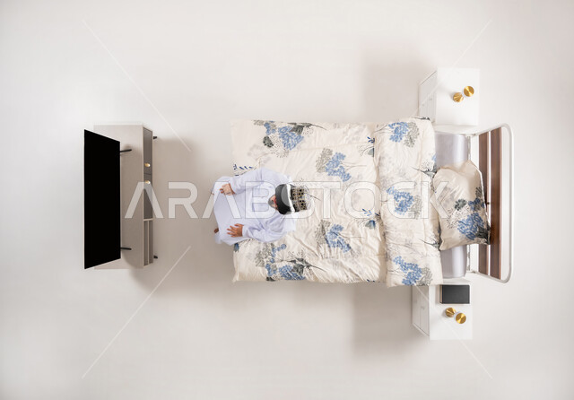 الاندماج ومحاكاة العالم الخيالي، الاستمتاع بمشاهدة أفلام الواقع الافتراضي، قضاء أوقات ممتعة ومسلية بالألعاب الافتراضية، بورتريه علوي عامودي لرجل عربي خليجي عماني يجلس على سرير مريح يرتدي الدشداشة والكمة ونظارات (الفي ار) ثلاثية الأبعاد، خلفية بيضاء