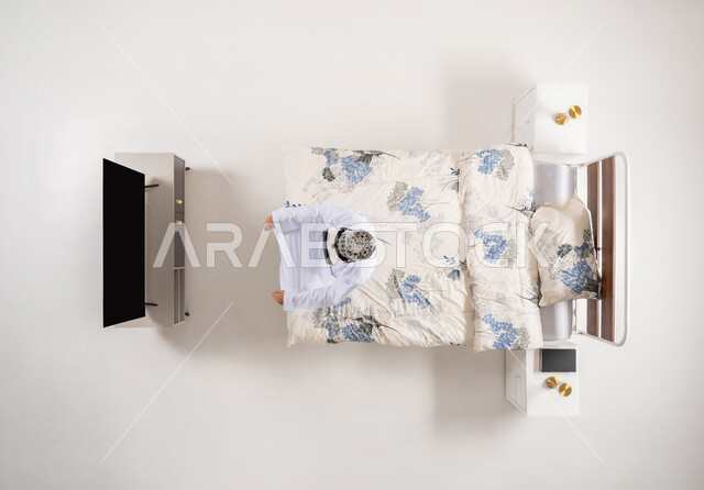 الاندماج ومحاكاة العالم الخيالي، الاستمتاع بمشاهدة أفلام الواقع الافتراضي، قضاء أوقات ممتعة ومسلية بالألعاب الافتراضية، بورتريه علوي عامودي لرجل عربي خليجي عماني يجلس على سرير مريح يرتدي الدشداشة والكمة ونظارات (الفي ار) ثلاثية الأبعاد، خلفية بيضاء